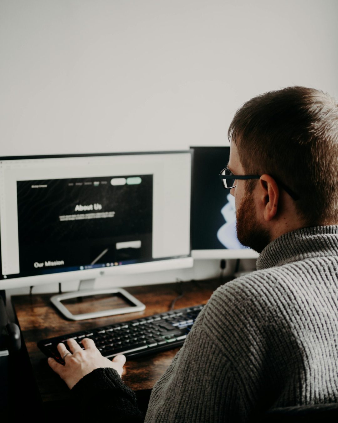 Man working on web design at home office setup with dual monitors.