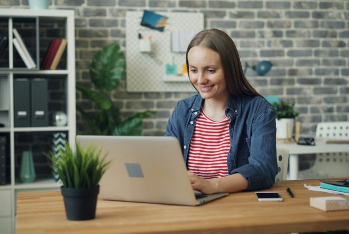 A woman uses a laptop at a stylish desk in a bright, modern office setting.