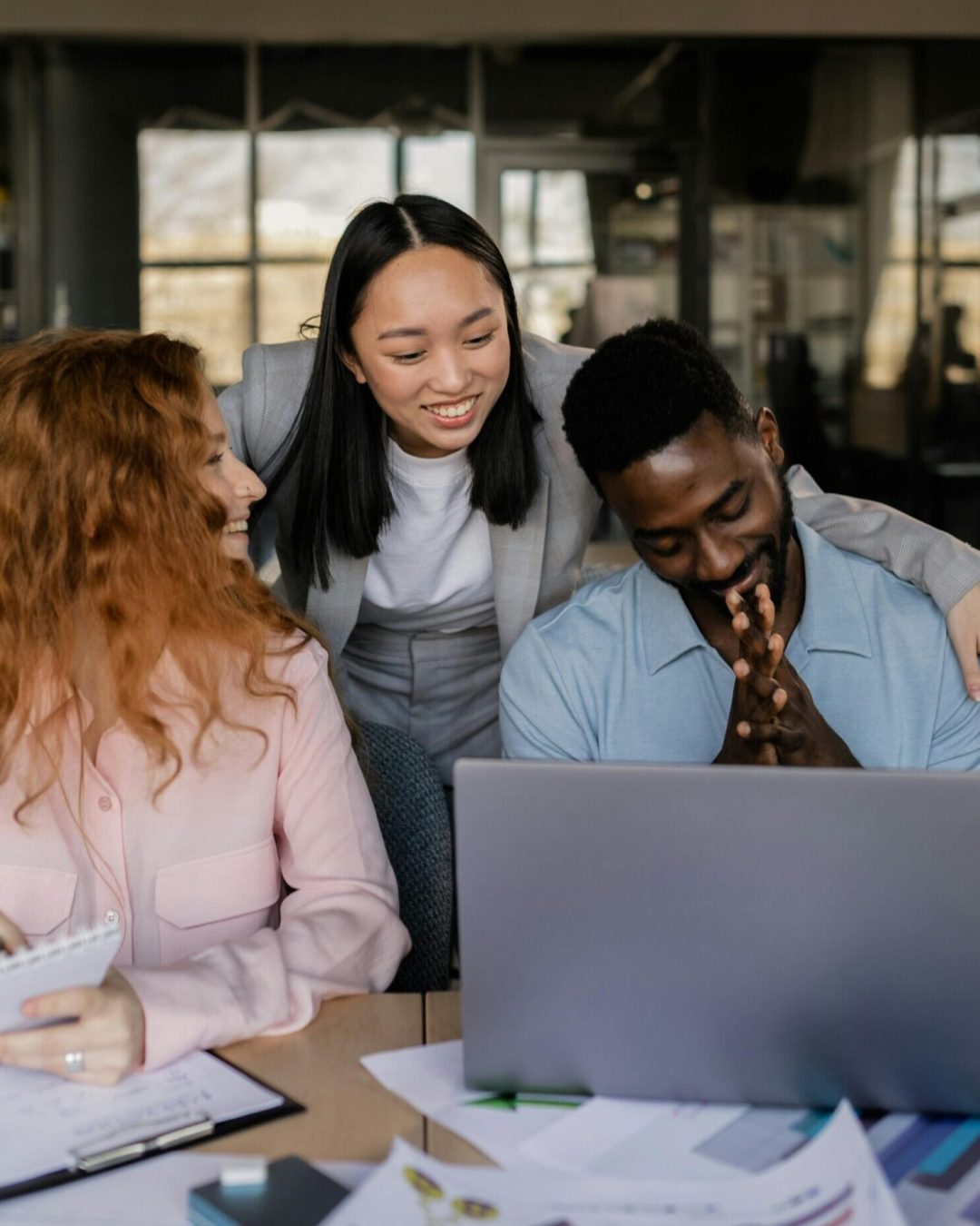A diverse group of adults collaborating on a project in a modern office, using a laptop and documents.